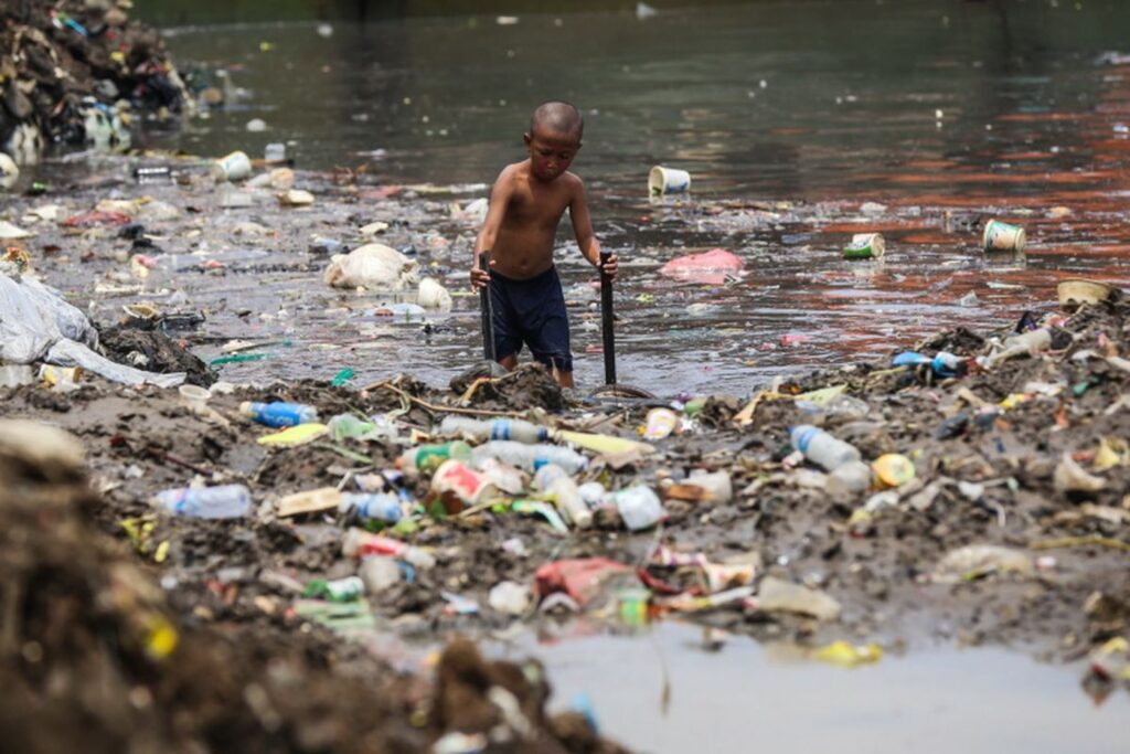 seorang anak kecil sedang membersihkan sampah plastik di sungai