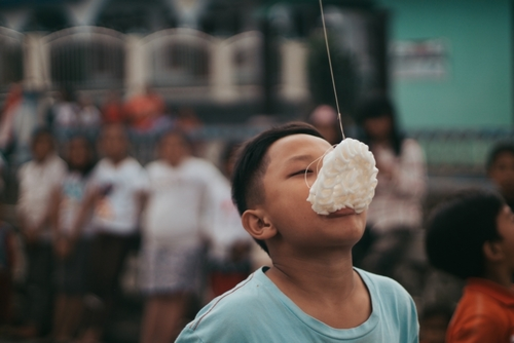Seorang anak laki-laki sedang mengikuti lomba makan kerupuk di 17 Agustus 2023
