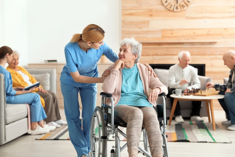 Seorang perawat sedang berbincang dengan lansia di atas kursi roda